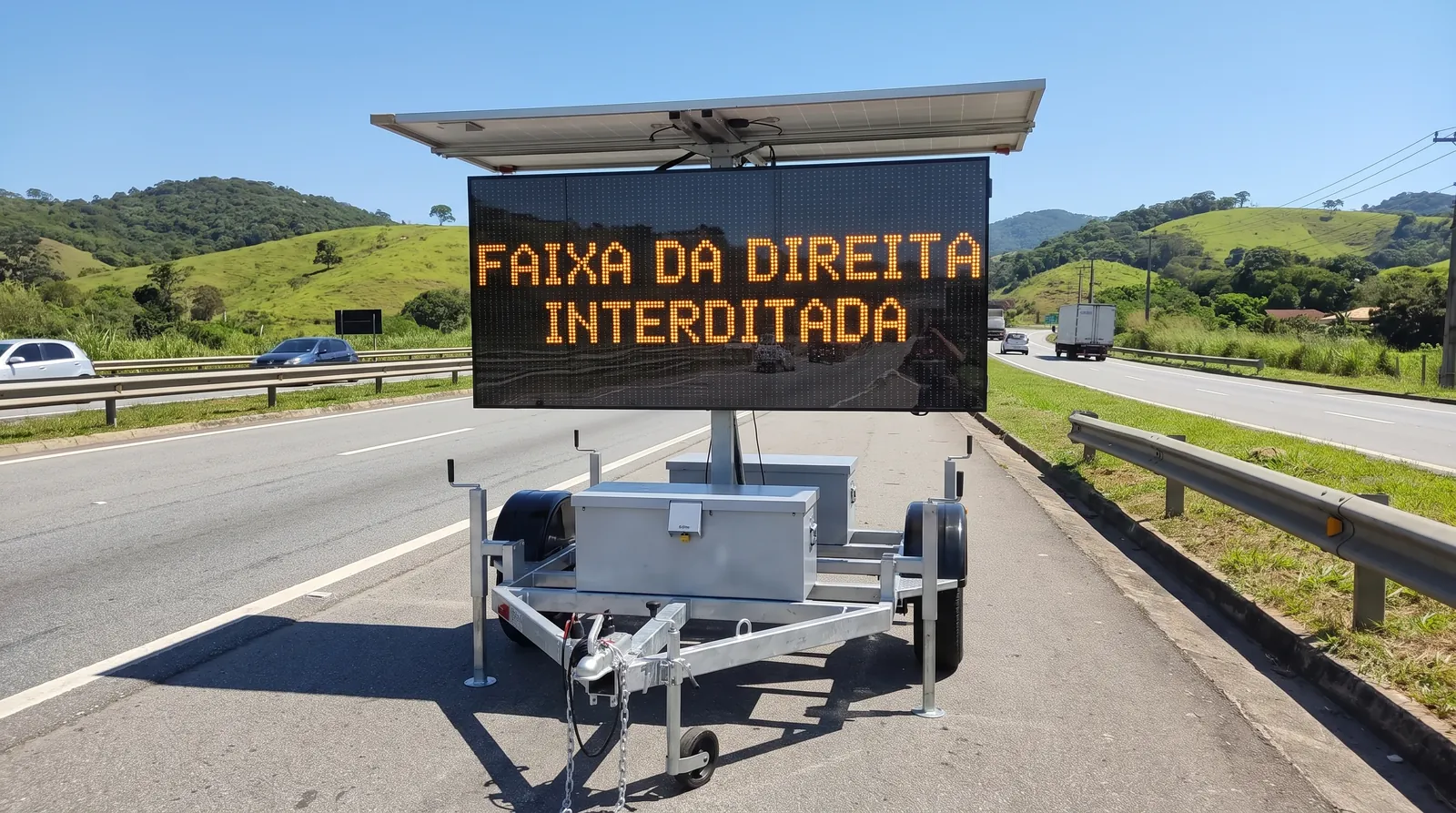 Painel de mensagem variável móvel exibindo FAIXA DA DIREITA INTERDITADA no acostamento de uma rodovia